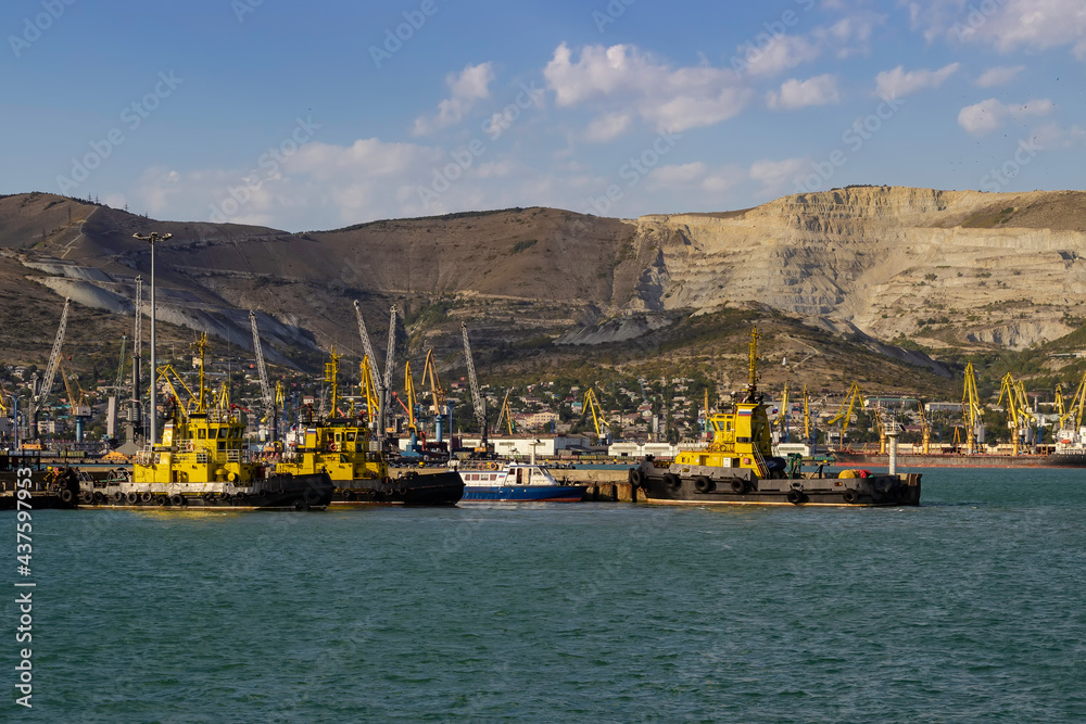 Harbor tugs stand at the pier against the backdrop of the mountains and the port.