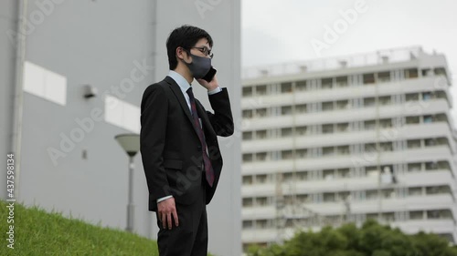コロナ禍に屋外でビジネスパーソンがマスクをして電話をしながら咳込む2