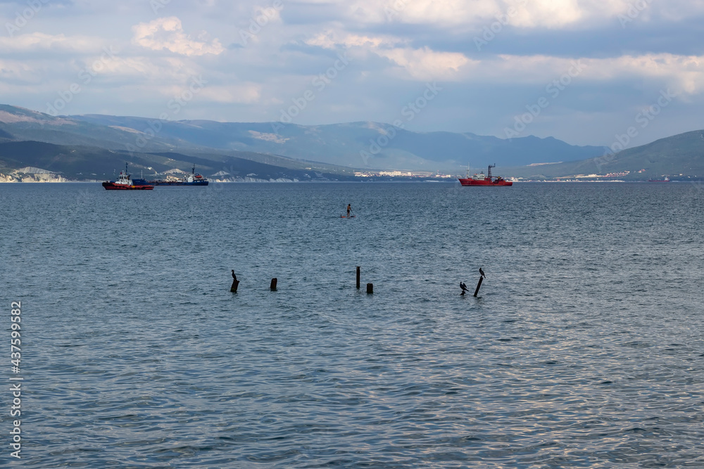 Obraz premium Pillars sticking out of the water into the sea. Ships and mountains in the background. The man on the boat in the center of the frame.