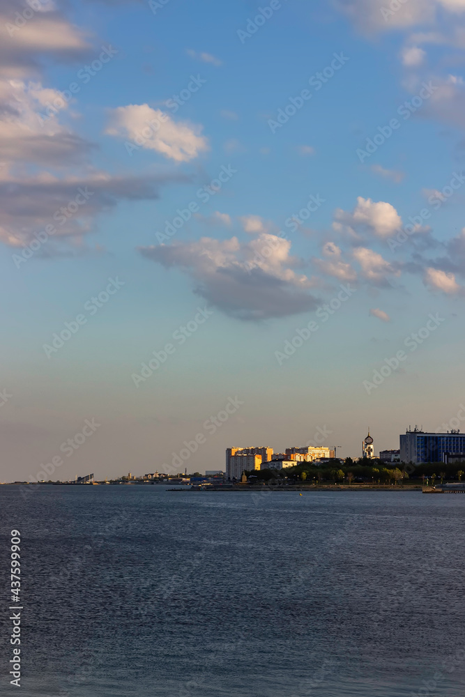 Coastline of a modern coastal town at sunset. Church and high-rise residential buildings on the seashore. Vertical orientation. Portrait orientation.