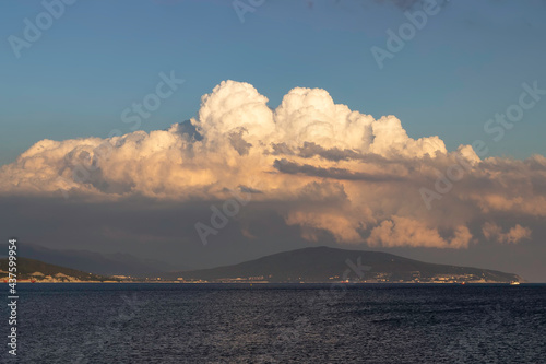 A small red ship sails along the bay against the backdrop of mountains and clouds.
