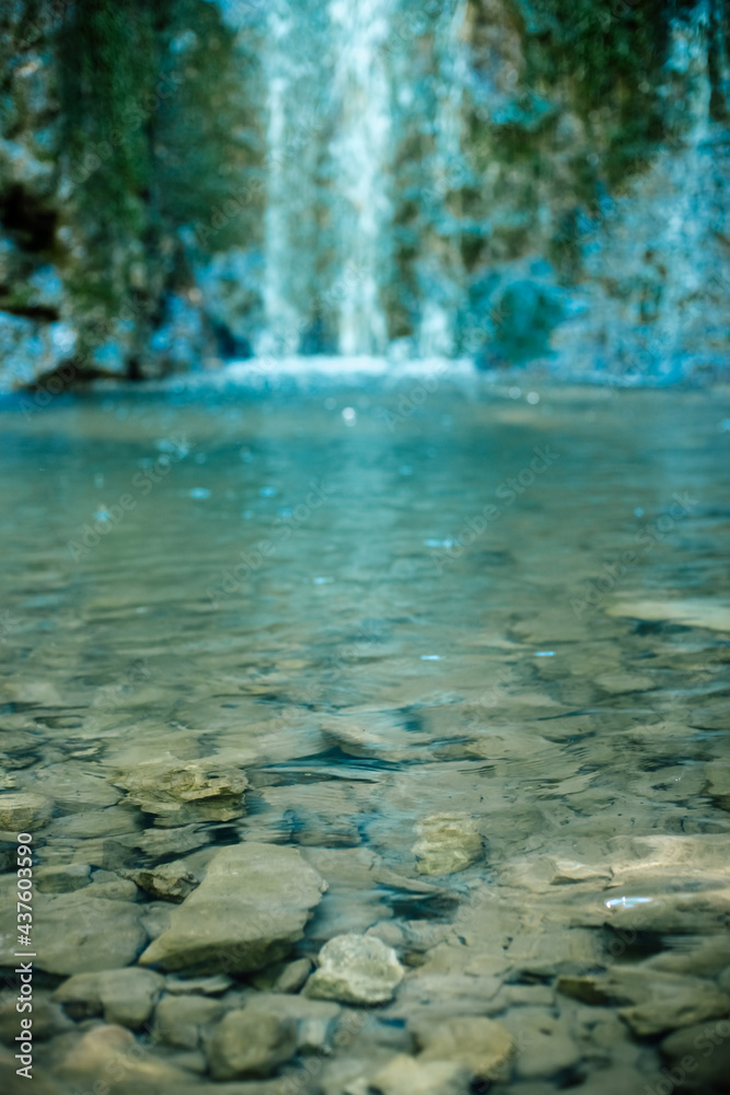 The rocky bottom of a mountain river against the backdrop of a small forest waterfall.
