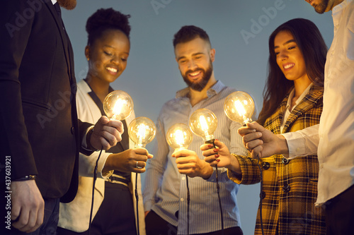 Fotografiet Group of happy young multiethnic people holding glowing lit retro Edison lightbulbs