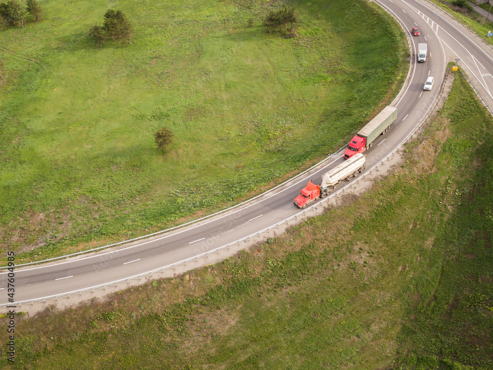 Dump trucks carrying goods on the highway. Red truck driving on asphalt road along the green fields. seen from the air. Aerial view landscape. drone photography. cargo delivery