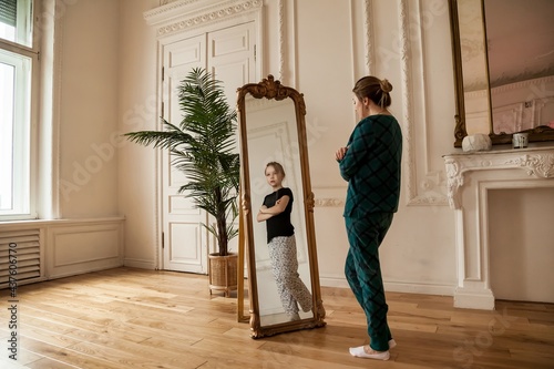 Middle age woman looking at mirror in living room and sees her daughter in reflection