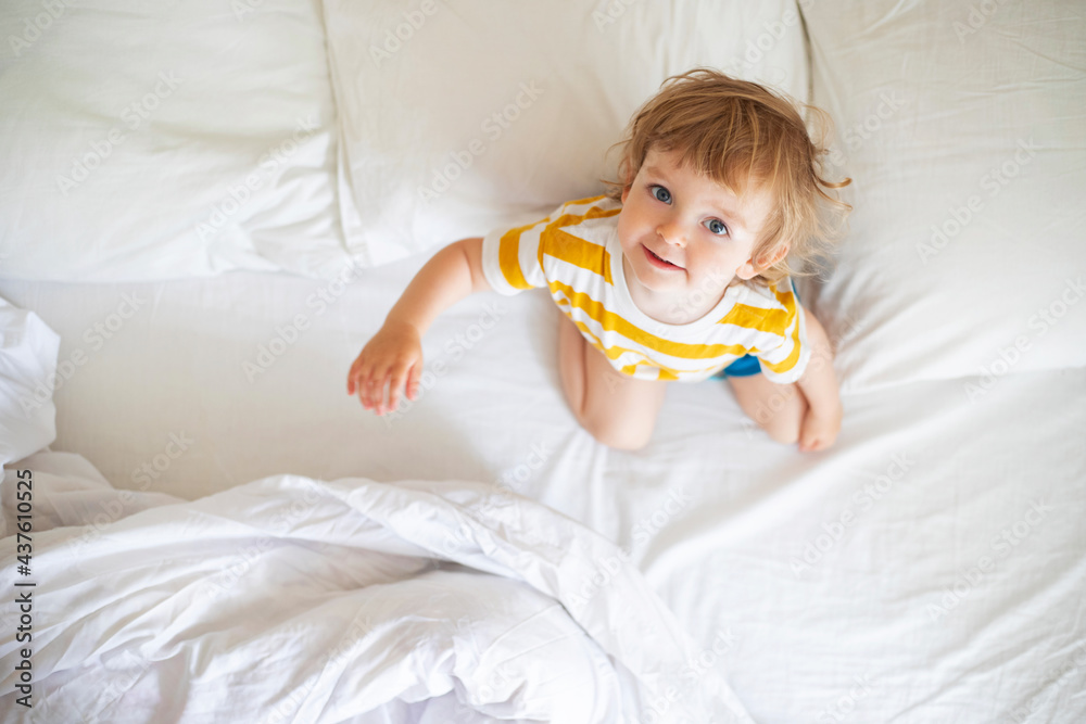 Top view of cheerful little boy in white bed early in the morning. Portrait of a handsome boy awakened Top view of cheerful little boy in white bed early in the morning. Portrait of a handsome boy awakened