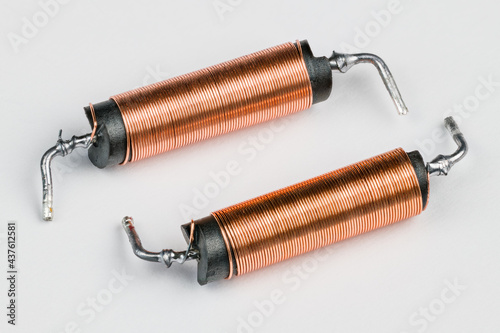 Two solenoids with helical copper wire wound on black coil on white background. Close-up of electronic components with magnetic field inside. Long cylindric inductors with ferrite core. Electromagnet. photo
