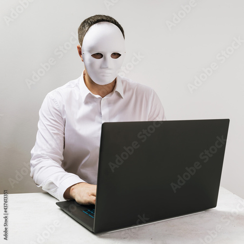 A man in a mask works behind a laptop, the concept of anonymity on the Internet photo