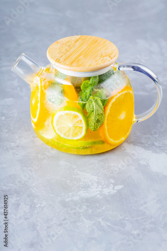 Detox lemonade drink of water, lemon, orange and mint leaves in a transparent teapot. Lime mint iced tea cocktail. Summer fresh drink. Copy space