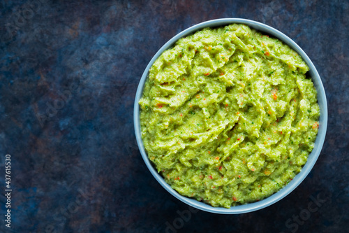 Guacamole in a gray bowl on a dark background. Bowl of avocado guacamole sauce with fresh ingredients. Copy space. Top view photo
