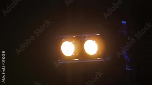 Two bright spotlights flash on stage, then flash brightly, in a loop