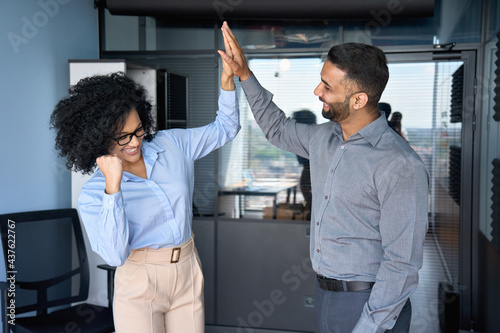 Cheerful successful coworkers colleagues indian businessman and African American businesswoman giving high five celebrating project victory in modern office. Business corporate culture concept.