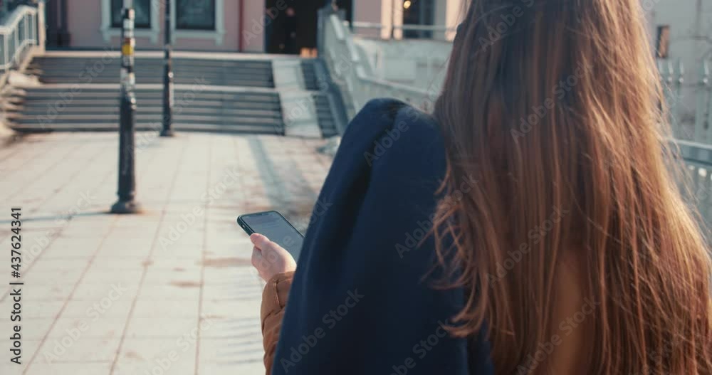 Camera follows young blonde business woman in face mask using smart phone while walking in city bridge on sunny day. Camera follows young blonde business woman in face mask using smart phone while walking in city bridge on sunny day.