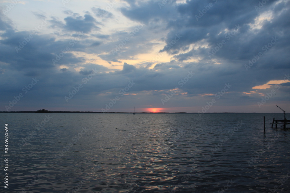 Gray clouds and pink sunset with a sailboat in the water