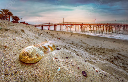 Large rock in sand pier in background southern california beach at sunset photo