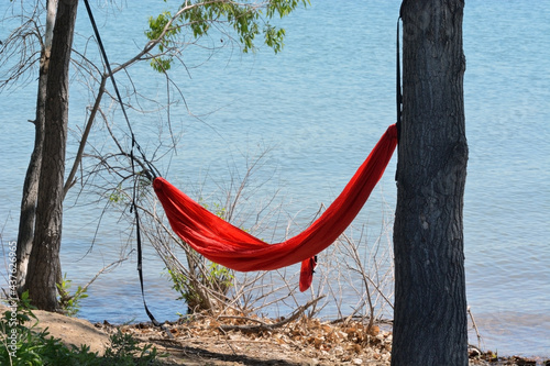 Orange hammock hung up between trees by edge of lake shore 