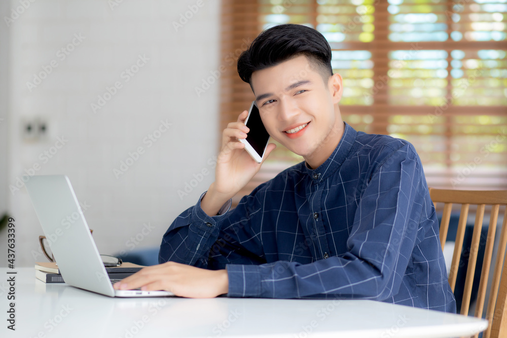 Young asian man talking phone and work from home with laptop computer, freelance using notebook to internet online and speak on smartphone, domestic life, business and communication concept. Young asian man talking phone and work from home with laptop computer, freelance using notebook to internet online and speak on smartphone, domestic life, business and communication concept.
