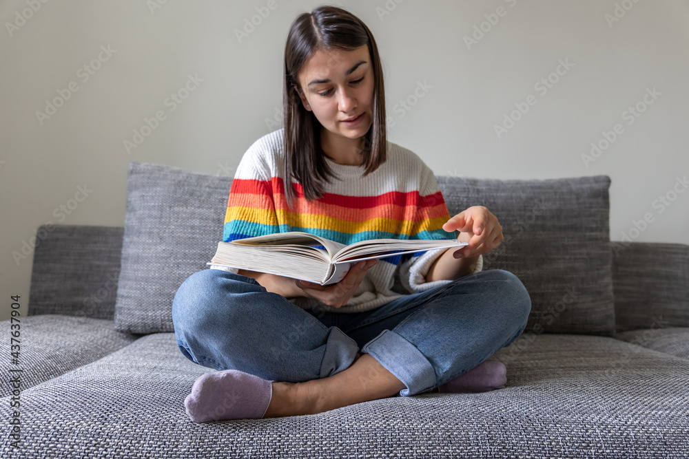 Young woman reads a book while sitting on the couch at home. Young woman reads a book while sitting on the couch at home.
