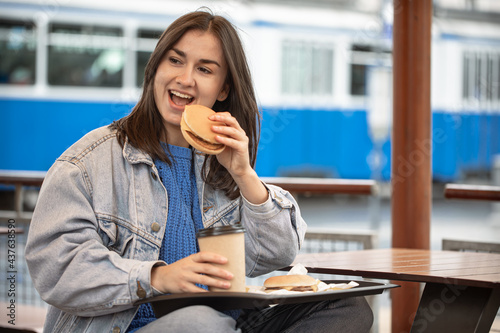 Street portrait of cheerful young woman eating fast food.