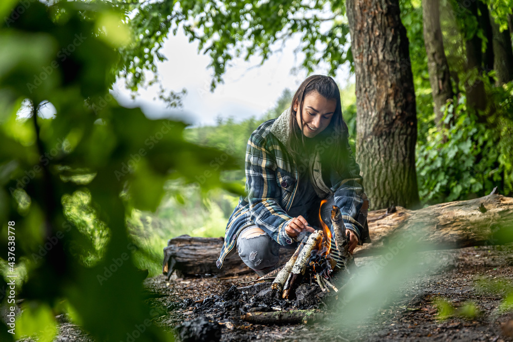 Fototapeta premium A cheerful girl in a hike in the forest makes a bonfire.