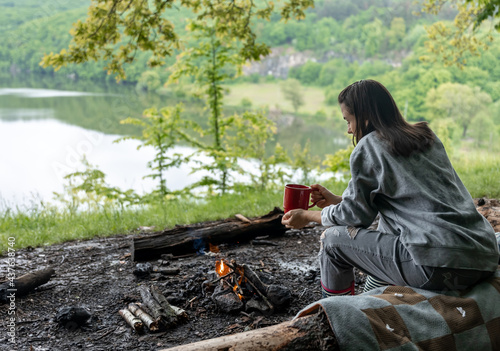 Girl with a cup of hot drink near the fire in nature.