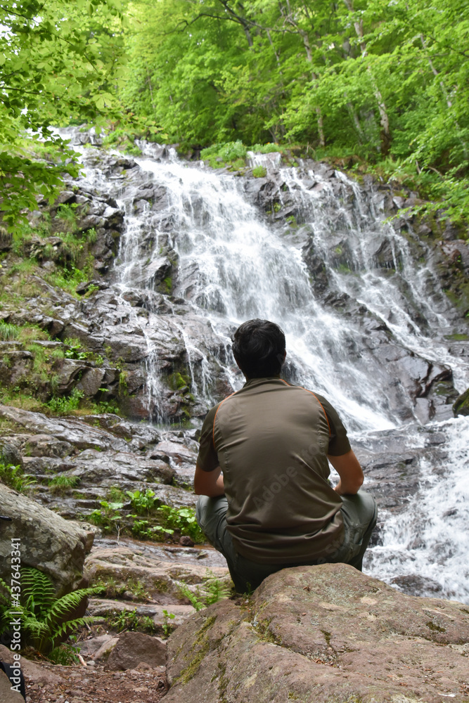 Adventurous man standing under the waterfall. Traveler looking at waterfall and enjoy in wind nature