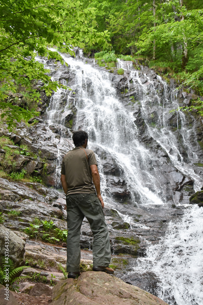 Adventurous man standing under the waterfall. Traveler looking at waterfall and enjoy in wind nature