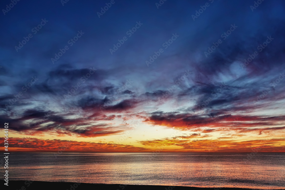Dramatic sunset over the sea. Dusk. There are purple and scarlet clouds in the blue sky. Orange glow over the horizon. Reflection on the surface of the water. Black Sea