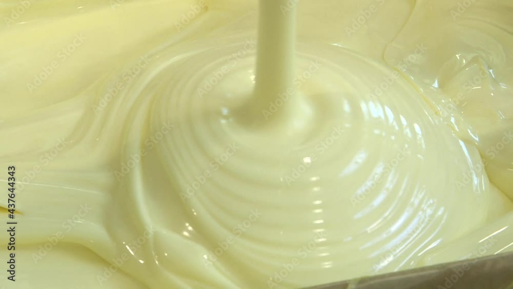The butter is poured into a box at the creamery. Close-up of a swirl of molten liquid cream. Dairy product. The butter is poured into a box at the creamery. Close-up of a swirl of molten liquid cream. Dairy product.