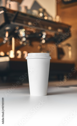 Big white clean cup of coffee to go on white table and professional coffee machine at the background blurred. Coffee concept mockup