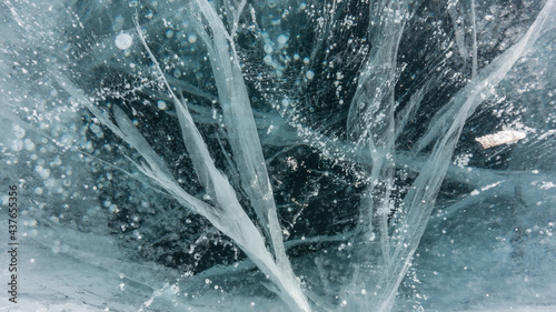 Turquoise ice close-up, detailed. The surface is lined with intersecting deep cracks. Bubbles of frozen methane gas are visible in the ice mass. Full screen. Baikal