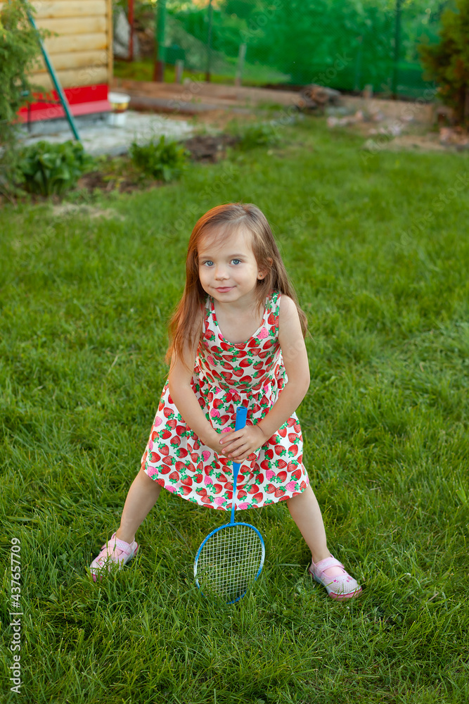 A girl with a racket on a green lawn. badminton. Active holidays in the summer. vacation. Vertical. Garden. A girl with a racket on a green lawn. badminton. Active holidays in the summer. vacation. Vertical. Garden.