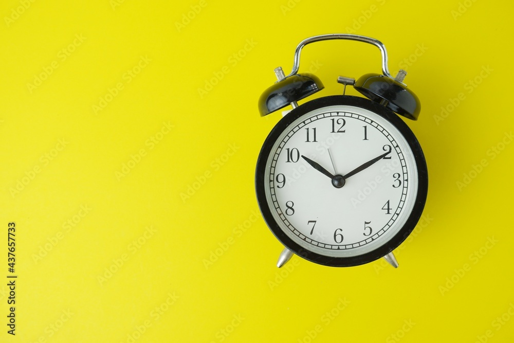 black alarm clock isolated on yellow background black alarm clock isolated on yellow background