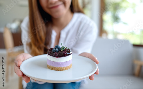 Closeup image of a young asian woman holding and showing a plate of blueberry cheesecake