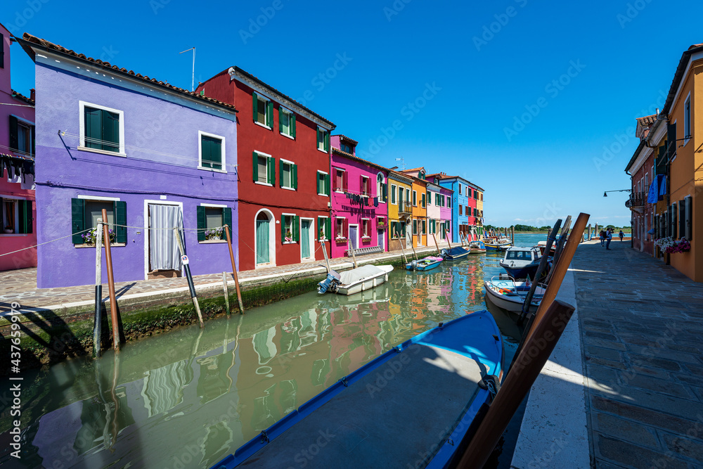 Burano island, Venice lagoon. Canal with small boats moored and beautiful multi coloured small houses (bright colors). UNESCO world heritage site, Veneto, Italy, Europe. On the horizon Torcello island