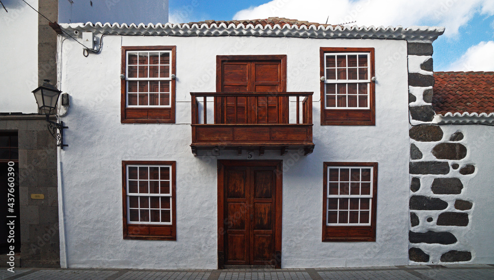 Picturesque facade of a large traditional stone house. White whitewashed wall. Red wooden doors, windows, balcony. Arabic style, La Palma, Canary islands