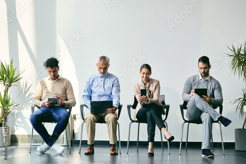 Group of job applicants using different digital devices while waiting for interview in the office. photo