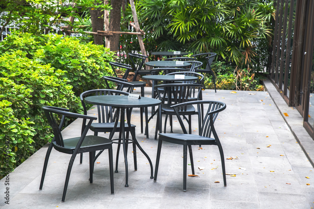 Black chairs and round tables set in the garden at a cafe, outdoor zone in Thailand, outside seating.