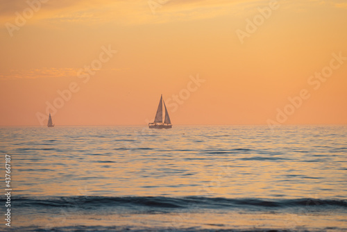 Sailing yacht on sunrise. Calm sea with sunset sky and sun through the clouds over. Ocean and sky background, seascape.