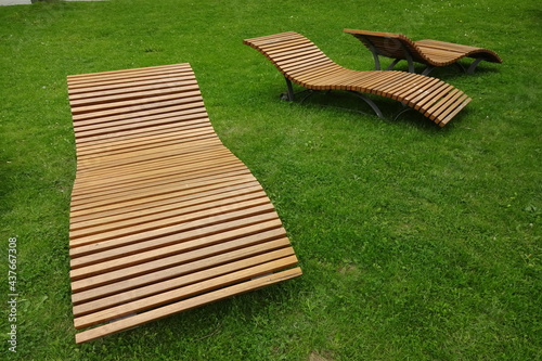 Tree isolated closeup curved empty benches on a green grass background or a backdrop in a park in summer or spring in Ulemiste, Tallinn. Bench made of wooden light brown planks. Relax or rest mood. photo