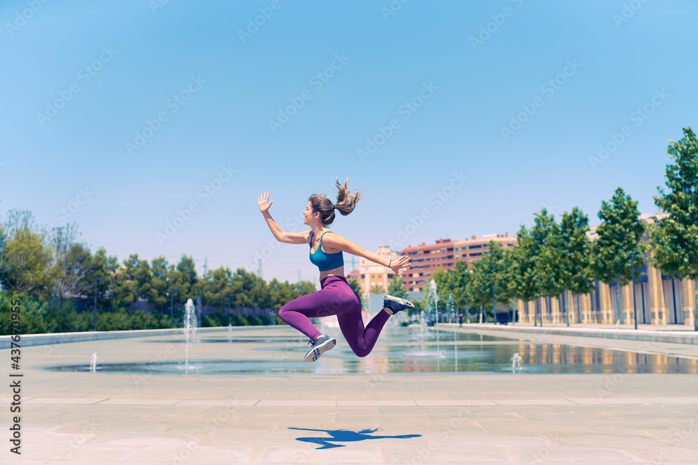 Young athlete jumps with joy. She is wearing sportswear. She has just finished her training and she is happy. Freedom concept.