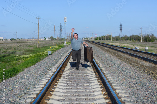 Man with suitcase runs along the railroad. Traveler missed his train and is catching up with him photo