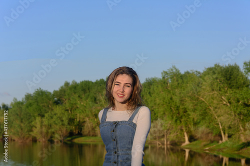 Portrait of young woman. Background of river and green forest in summer at sunrise. Happy mood © NataliaSavilova