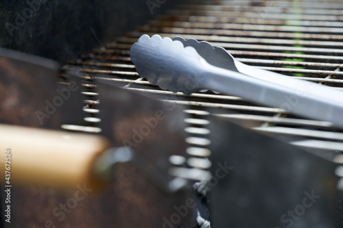 Part of a stainless steel grill tongs on a dirty grill rust. Wooden handle blurred in the foreground. Side view. Depth of field.