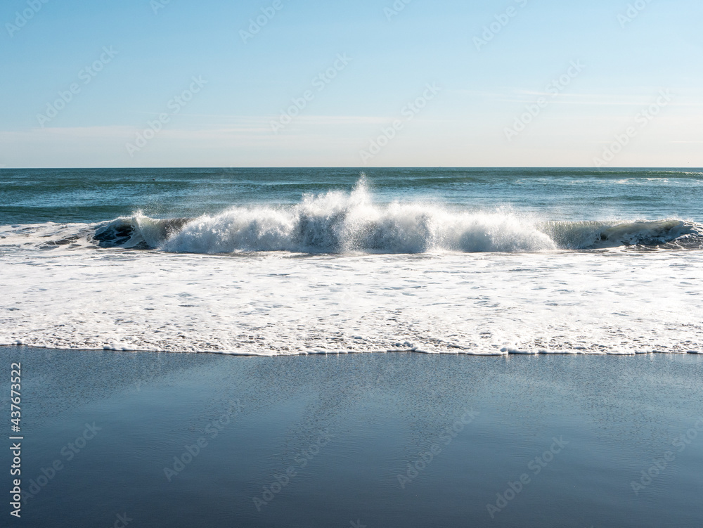Fototapeta premium View from the Khalaktyrsky beach to the Pacific Ocean against the background of the blue sky. On the shores of the black sand beach, big and small waves break. Kamchatka Peninsula, Russia.