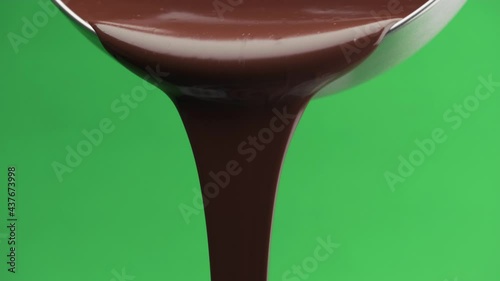 Melted black chocolate pouring from a metal bowl isolated on a green screen background, chroma key. Template for motion design or advertising.