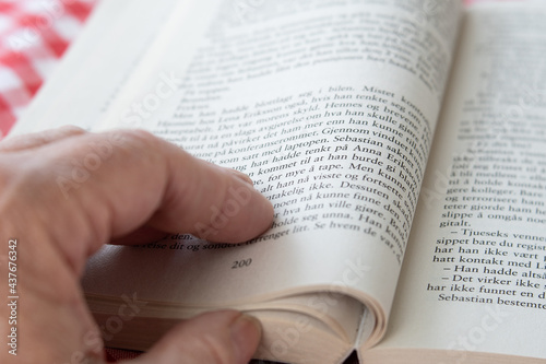  Person reading a book. Close up of the left hand and pages.blurred and sharp areas.