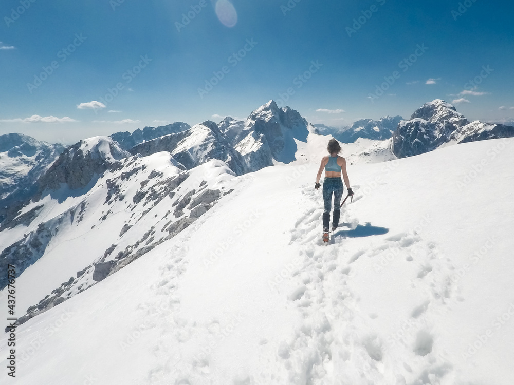 slender positive girl climber mountaineer with ice axe on a snowy alpine slope