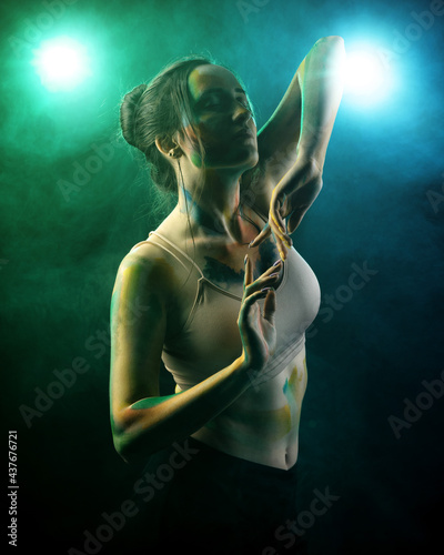 A girl with paint on her body stands against a backdrop of smoke, consecrated by blue and green light © ISliM