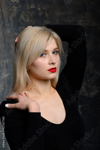 Young blonde plump woman with bright makeup in black bodysuit at dark background